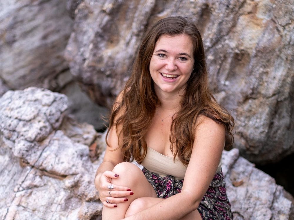 Mary Tichelaar laughing, sitting on a rock with her arms around her knees